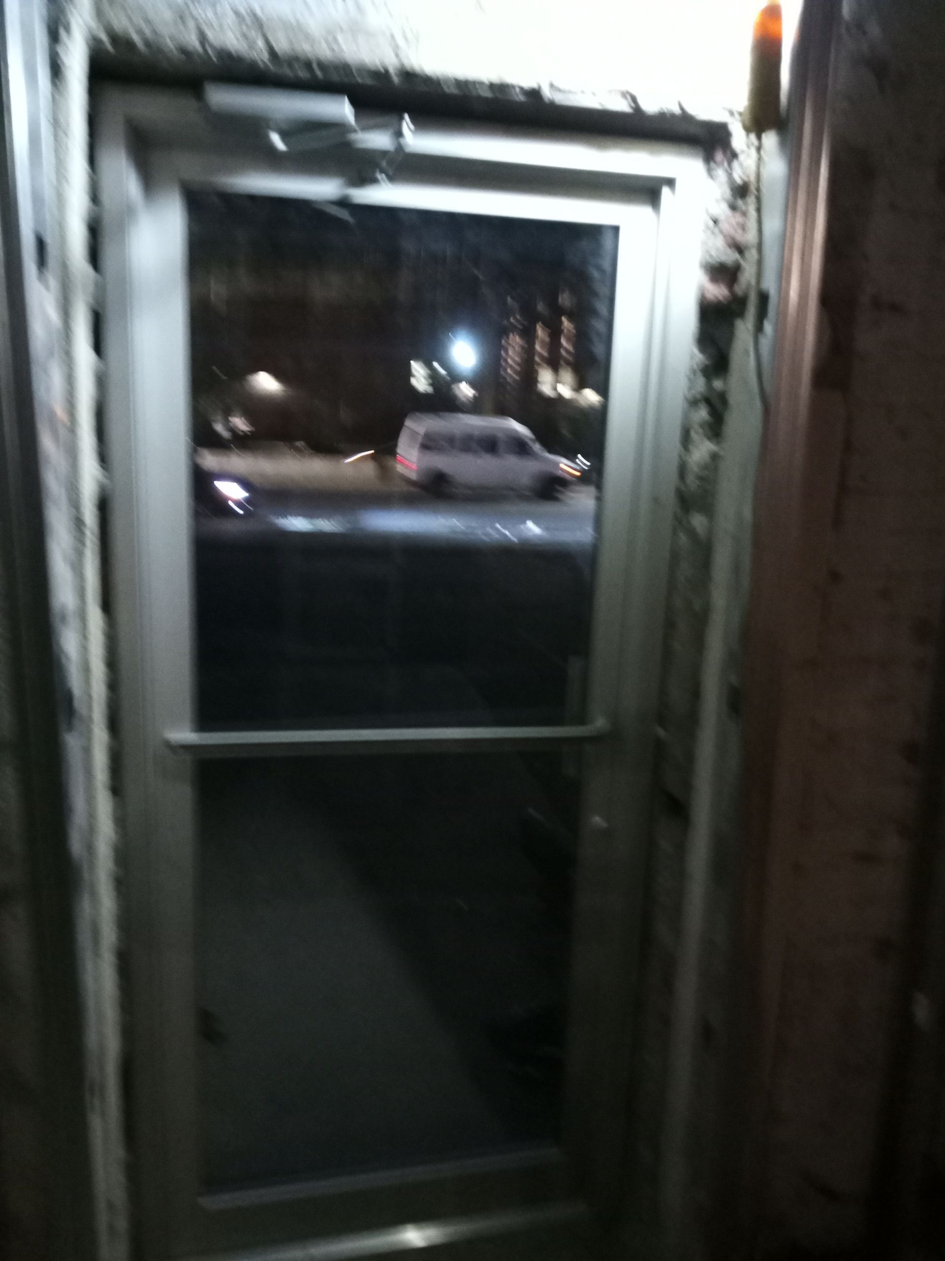 Narrow doorway at night, looking out to a parked white van and streetlights outside.
