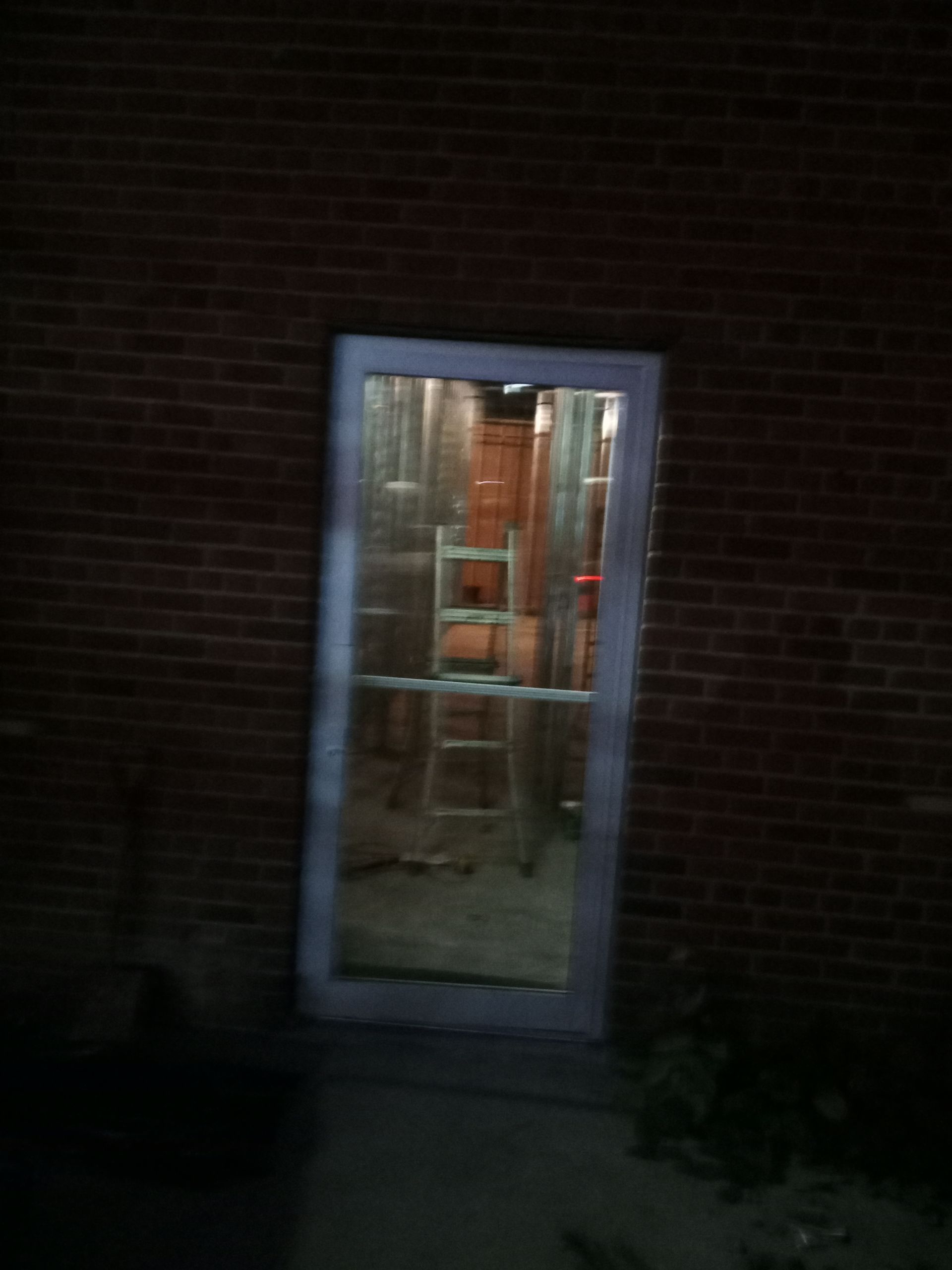 Dimly lit doorway in a brick wall, showing a room with shelves and a red chair inside.