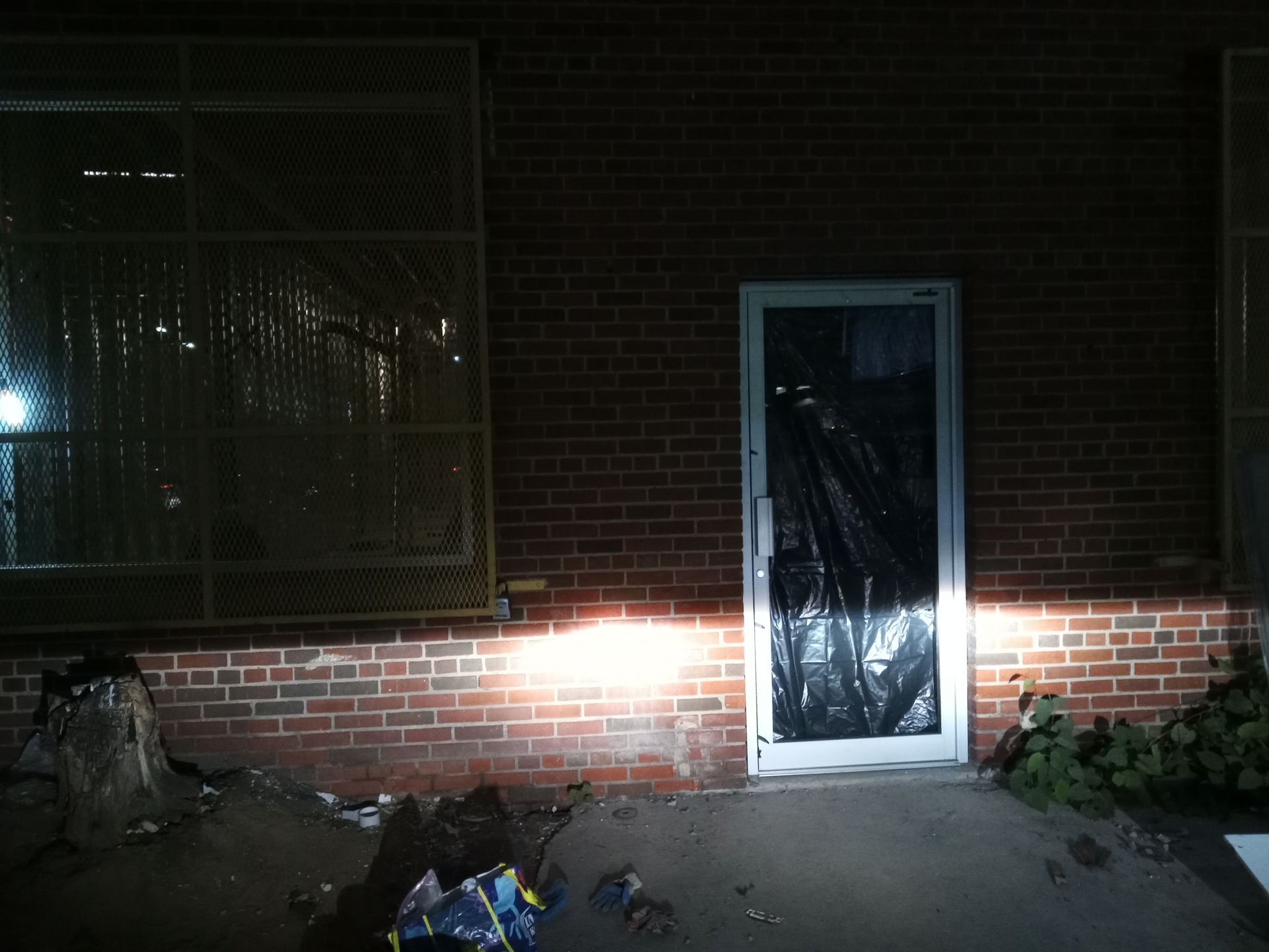Dimly lit brick building entrance with a taped-over door and bright light shining across the wall.