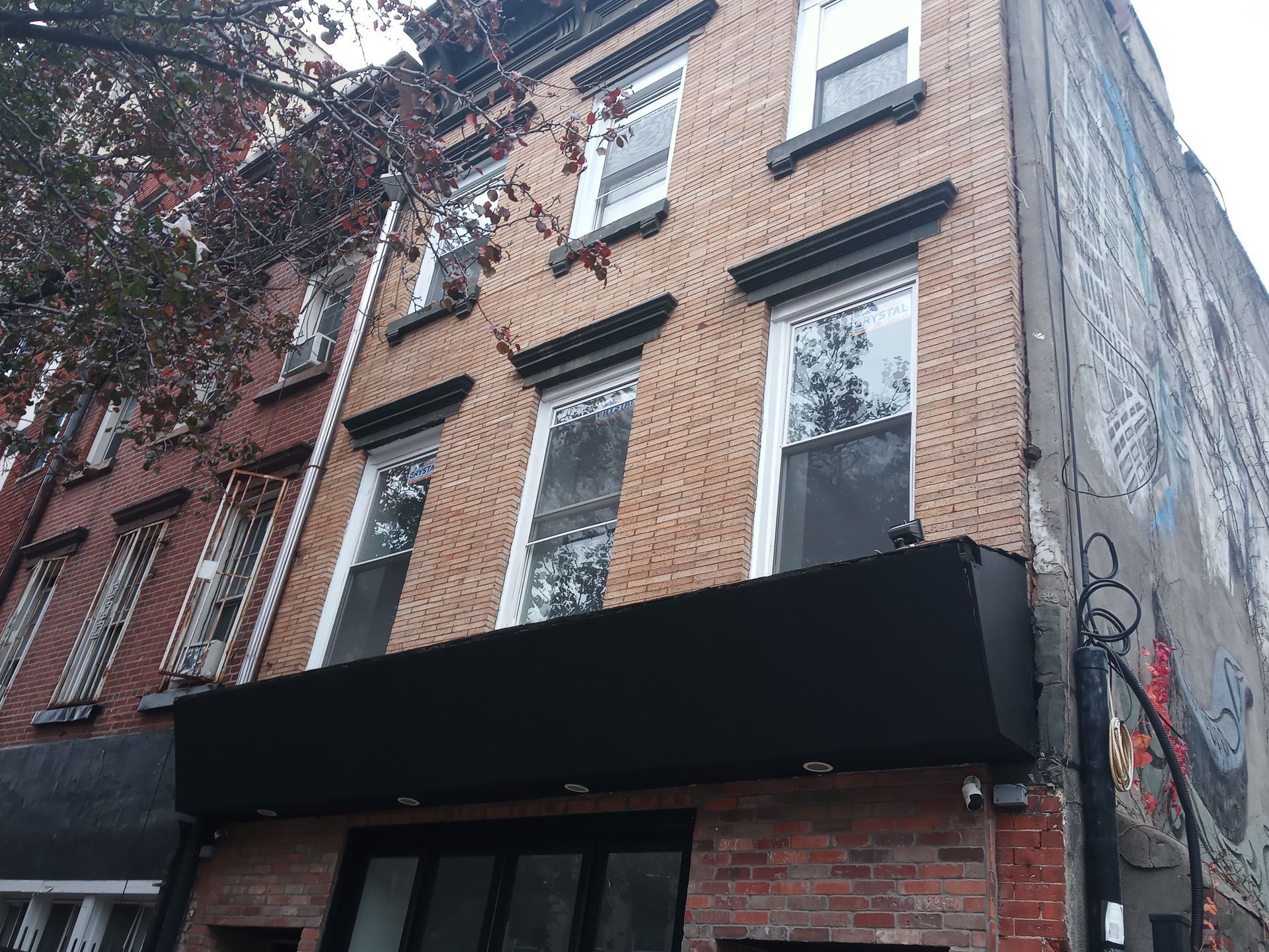 Brick apartment building with black awning and fire escape, viewed from below on a city street