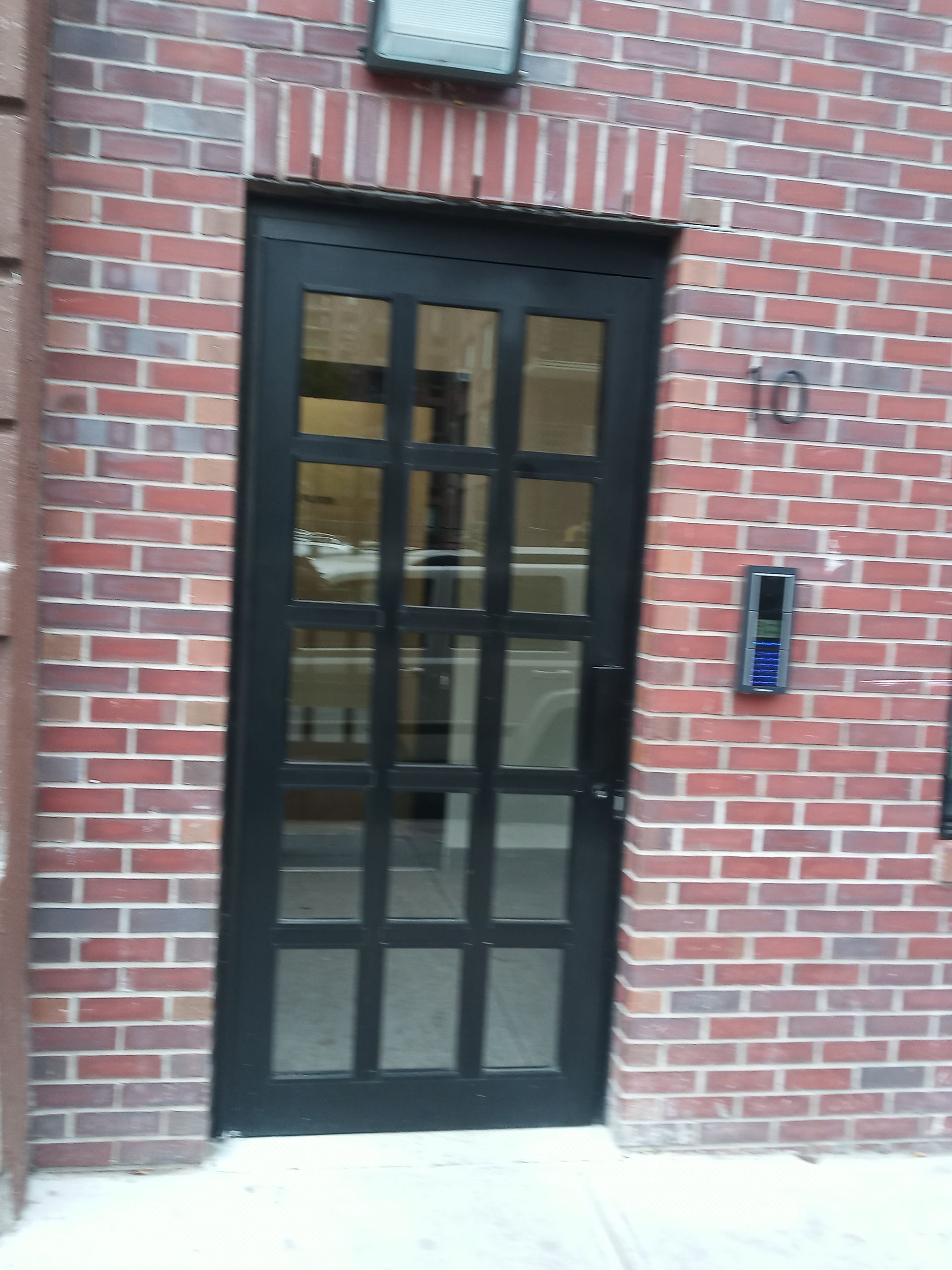 Black-framed glass door set in a red brick wall with an intercom panel beside it.