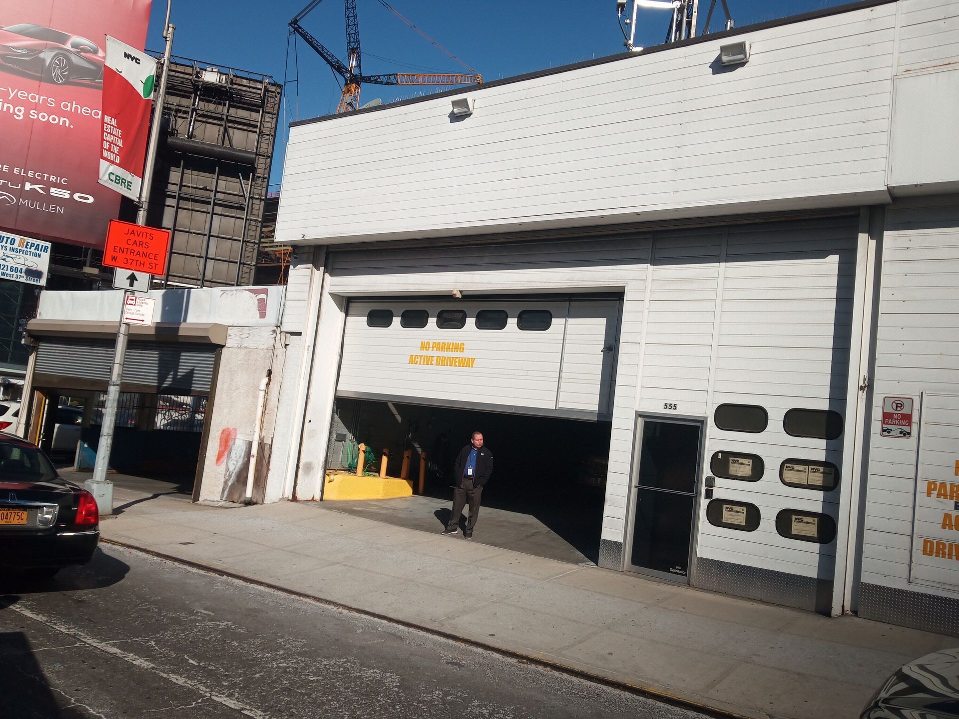 White garage-style storefront with an open bay, a person standing outside, and cars parked along the street.