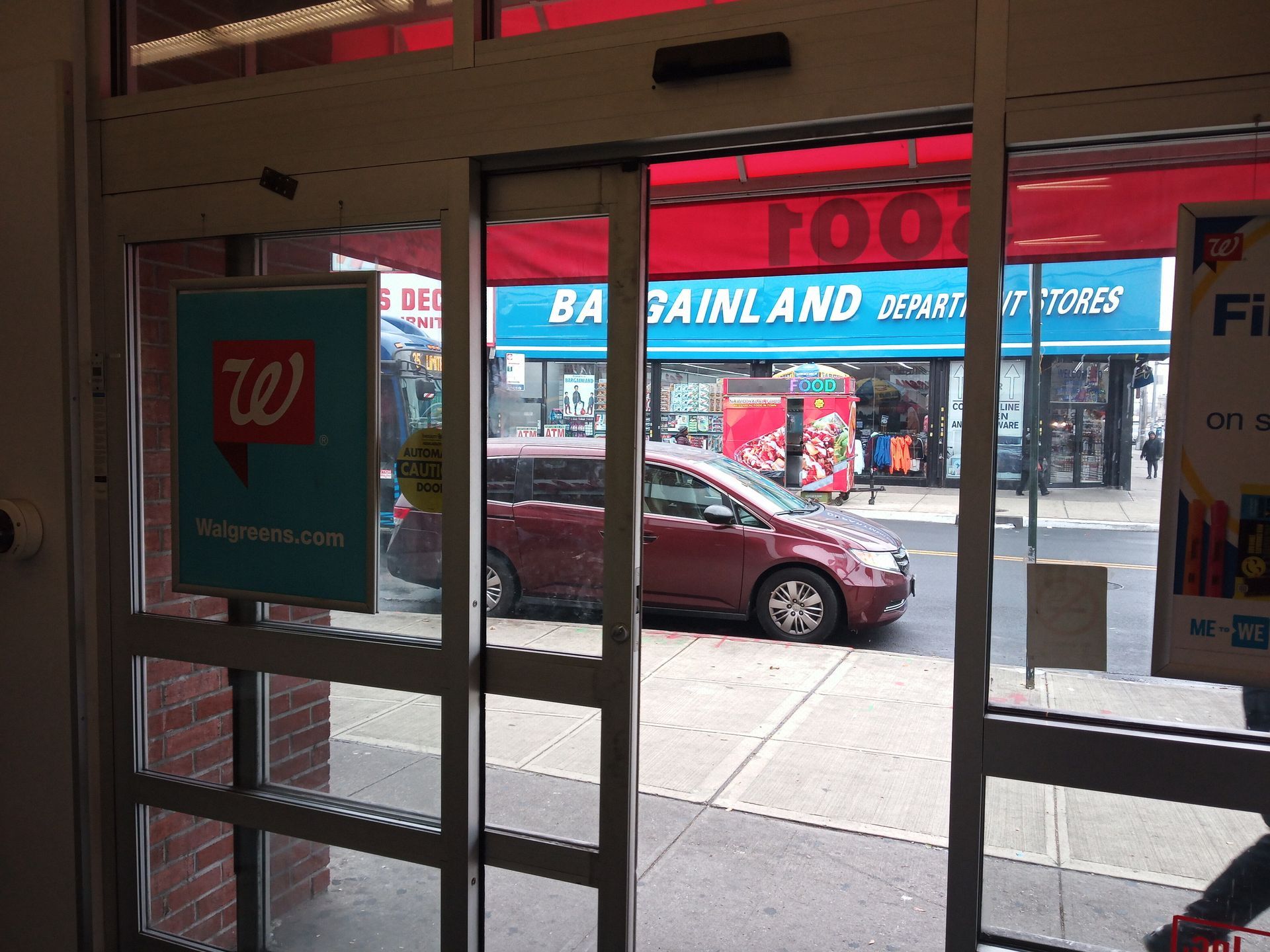 Store entrance with glass doors looking out onto a street and parked cars.