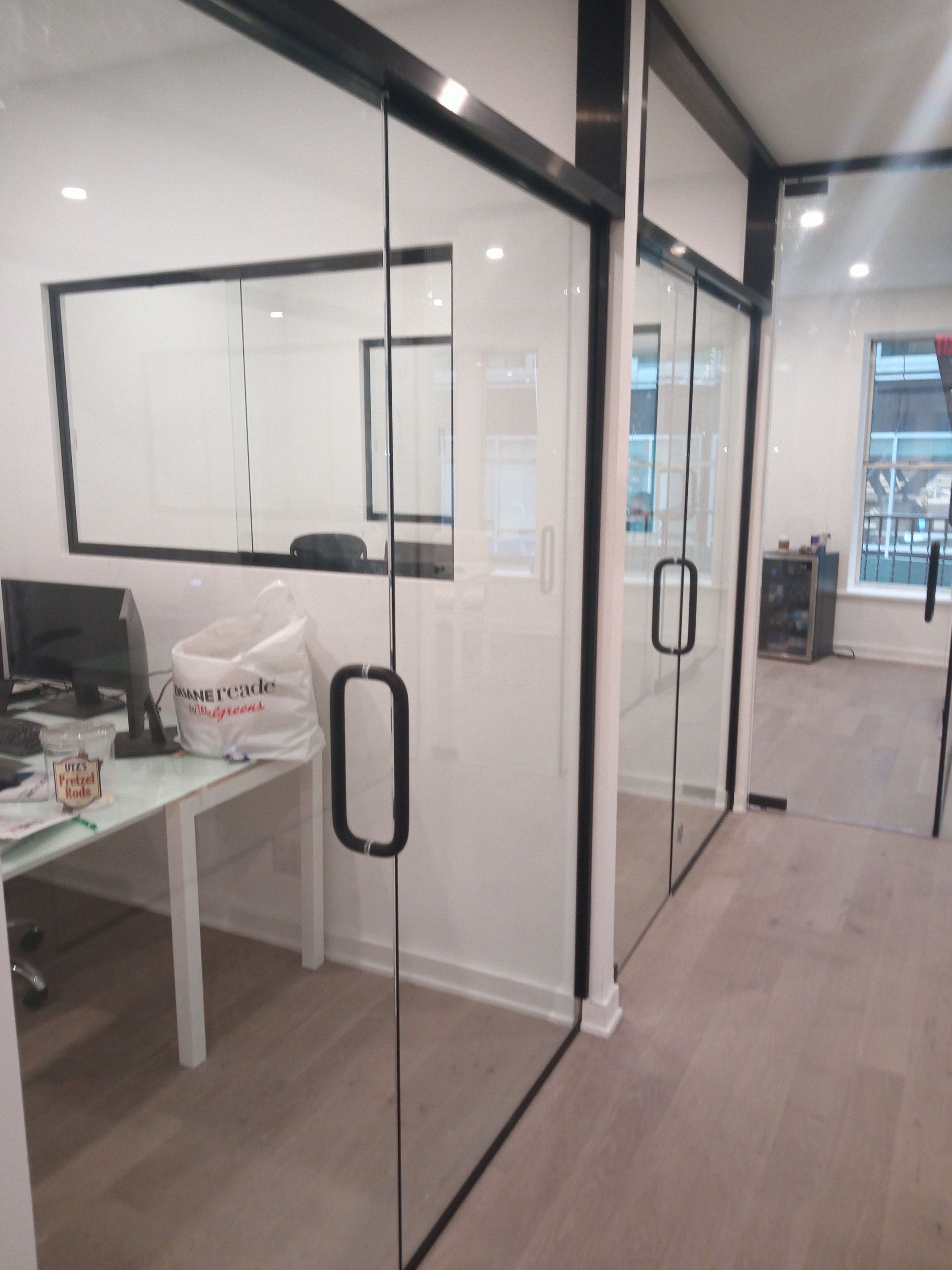 Modern office hallway with glass sliding doors, white desks, and an open workspace beyond.