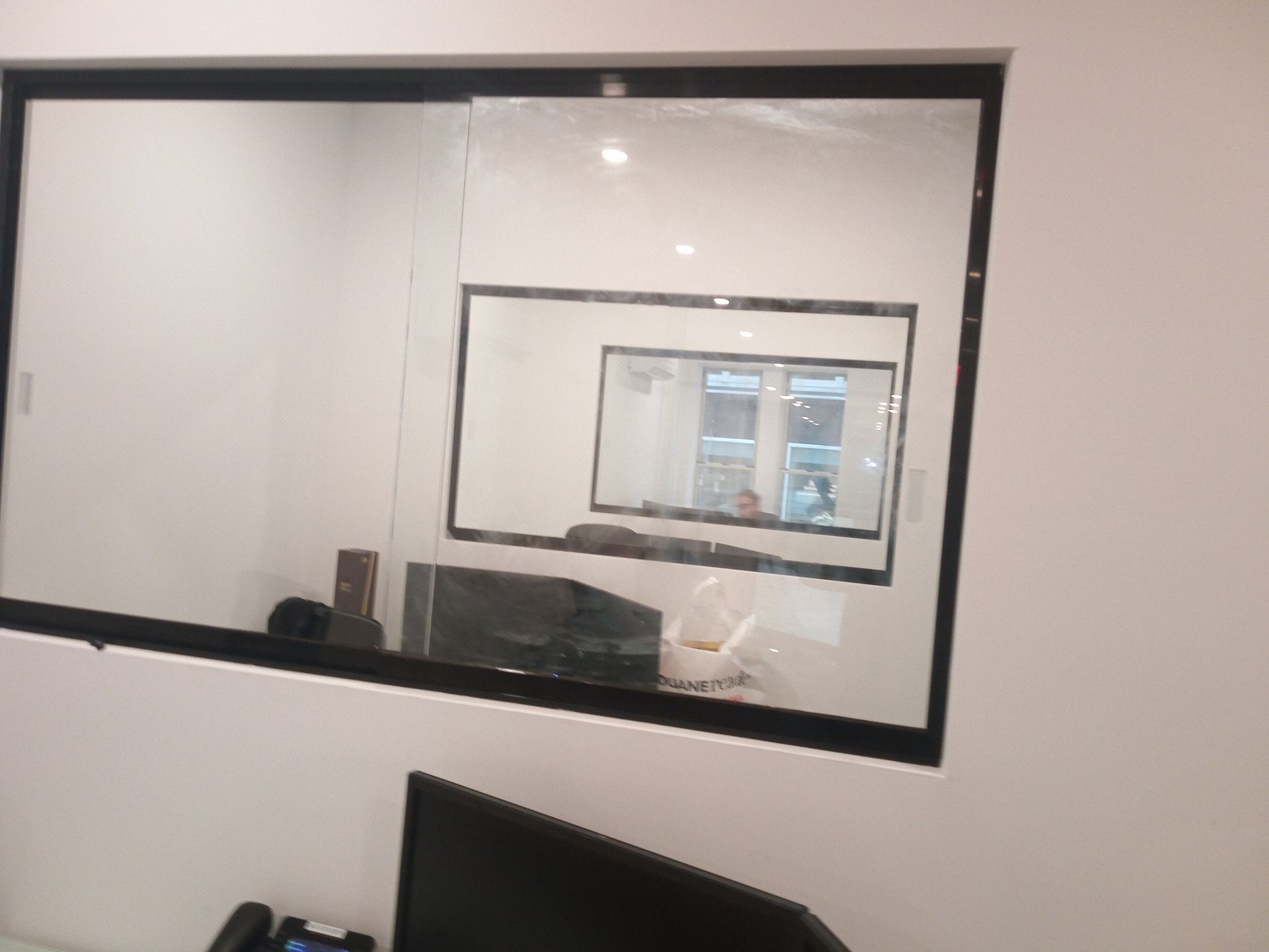 Office conference room with glass window and door, showing a monitor reflected on the wall.
