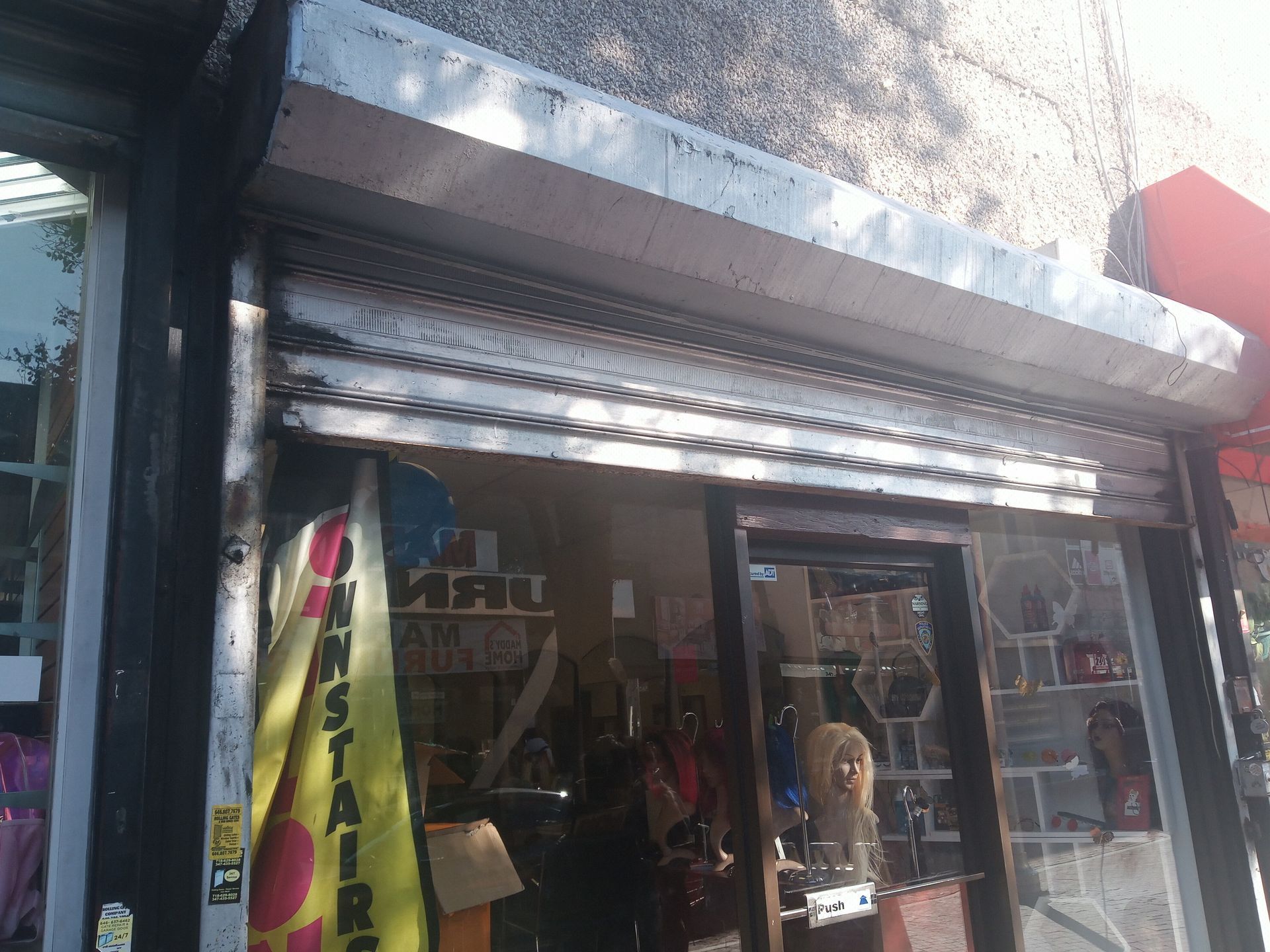 Storefront with a metal shutter, mannequins in the window, and a yellow sale banner outside