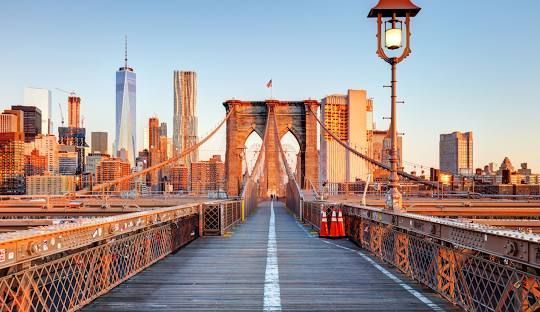 Brooklyn Bridge walkway at sunrise with Manhattan skyline in the distance