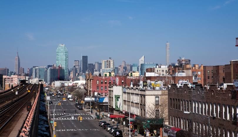 City skyline over a busy street, with red-brick buildings and elevated tracks under a clear blue sky