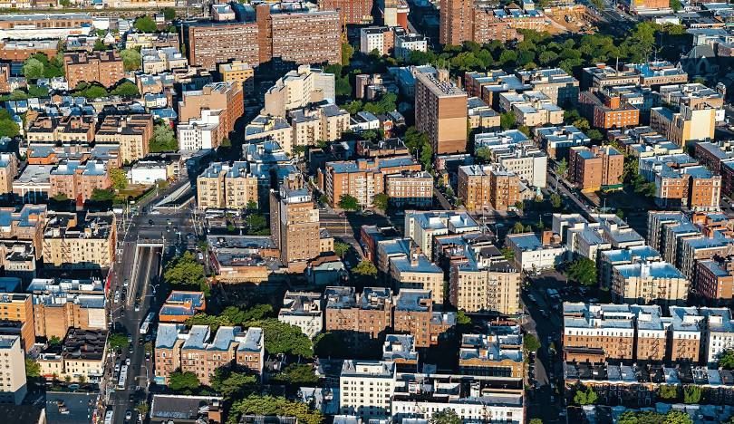 Aerial view of a dense urban neighborhood with apartment buildings, streets, and parked cars.