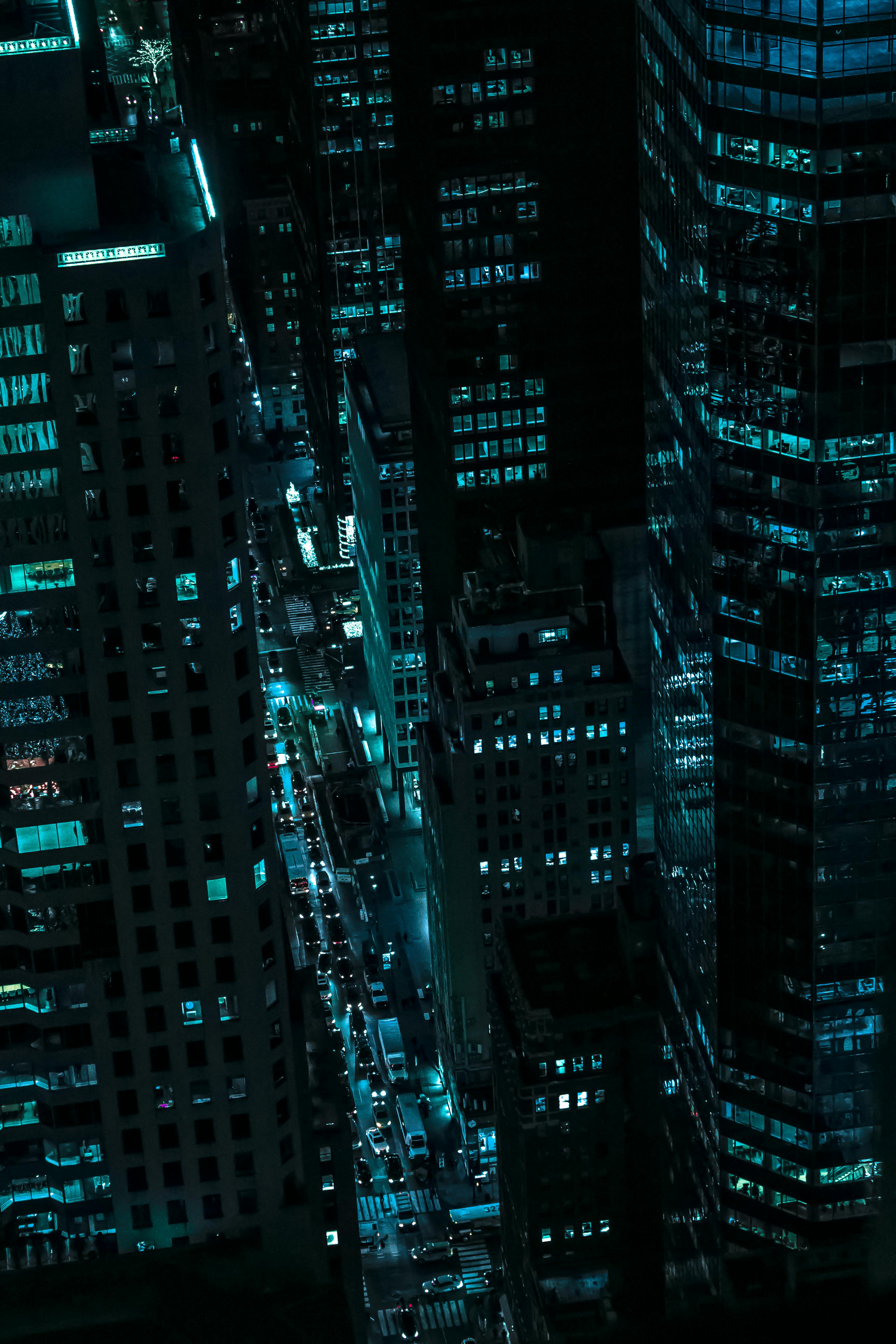 Aerial view of tall city skyscrapers at night with glowing turquoise windows