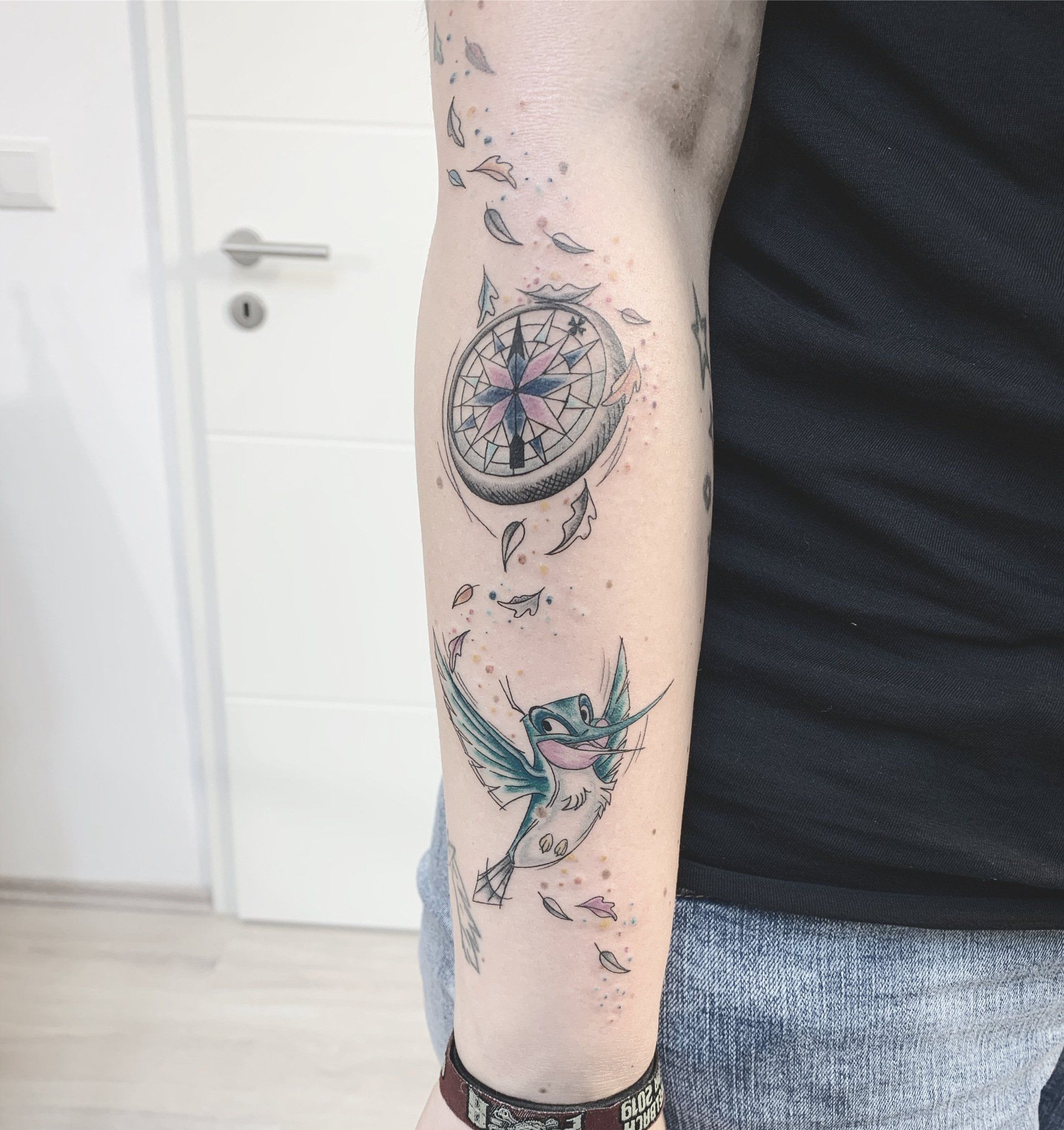 Tätowierung auf einem Arm: Kompass, fliegender Vogel, verstreute Punkte und Linien.