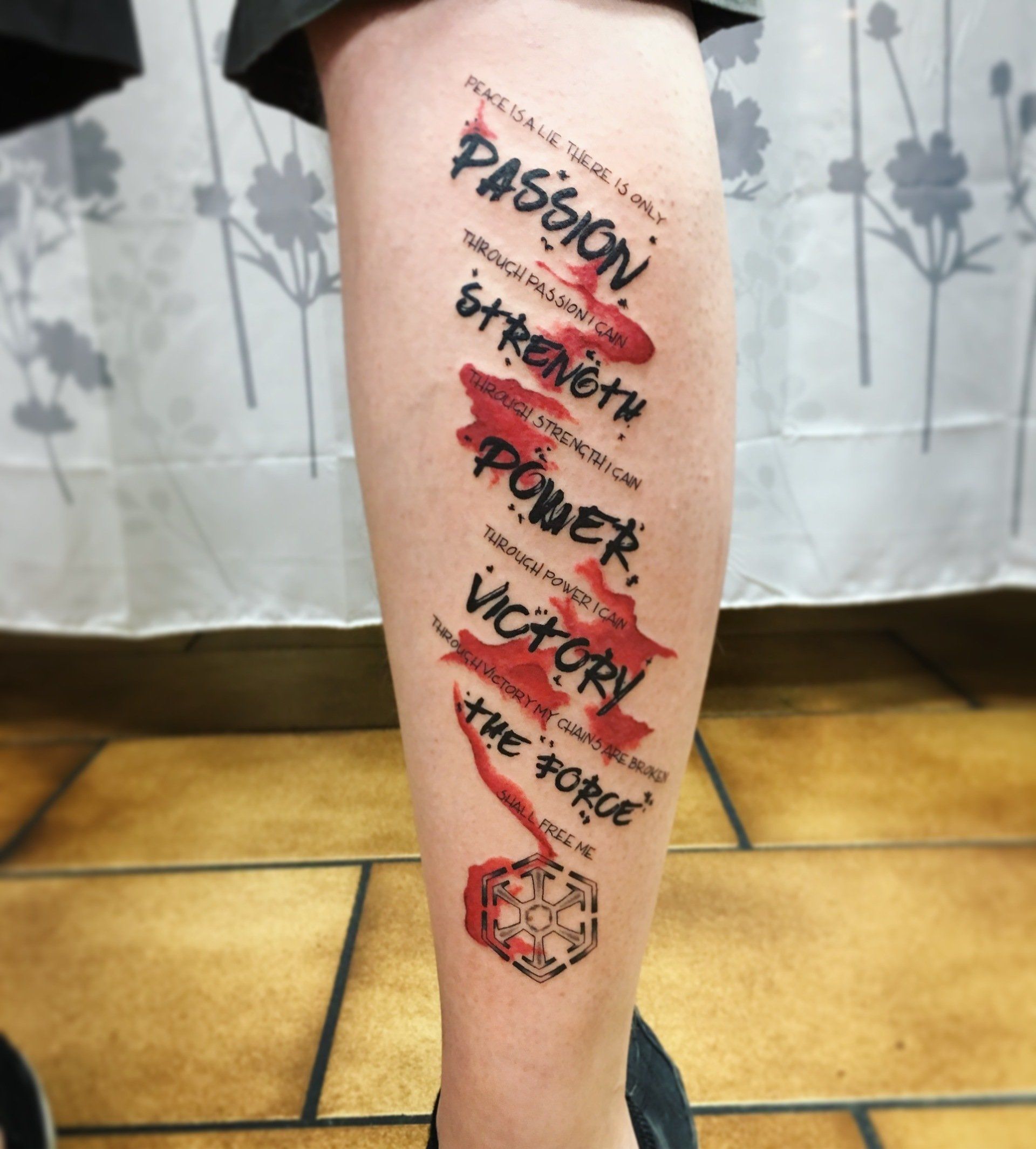 Tätowierung der Worte „Leidenschaft, Stärke, Macht, Sieg, Die Macht“ mit roten Streifen auf einem Bein und einem Star Wars-Symbol.