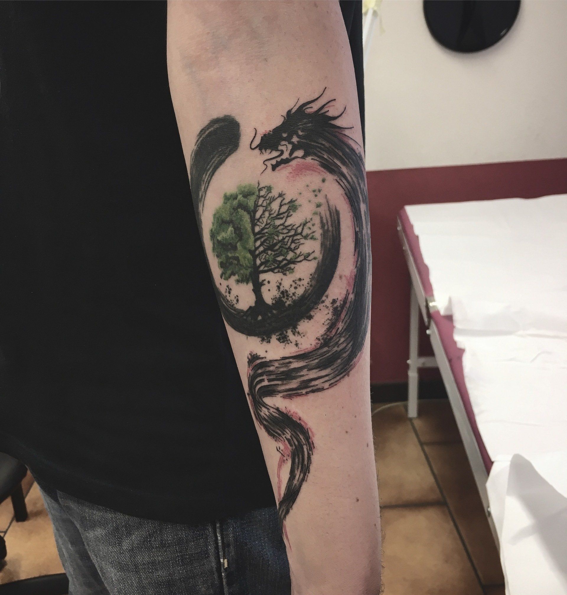 Tätowierung eines schwarzen Drachen, der sich um einen Baum innerhalb eines Zen-Kreises windet, auf einem Arm.