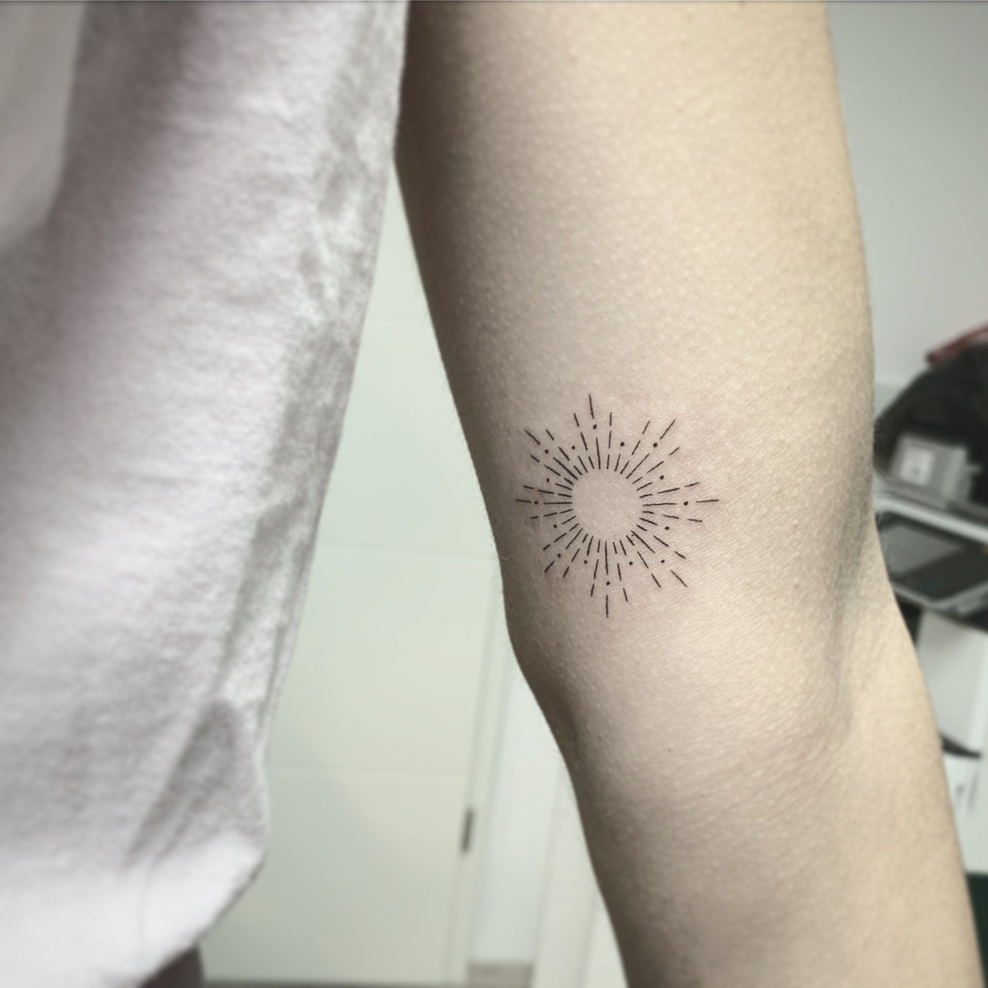 Sonnenstrahl-Tattoo am Ellbogen mit strahlenförmigen Linien und Punkten.