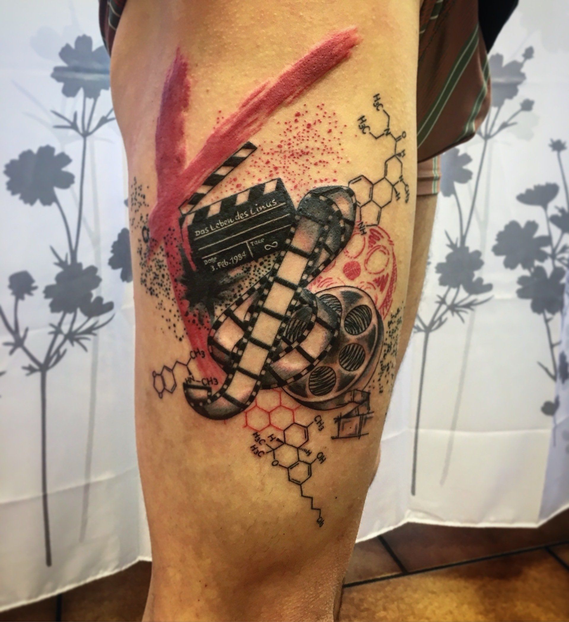 Tattoo mit Filmrolle und Filmklappe mit roten Akzenten auf dem Oberschenkel einer Person.