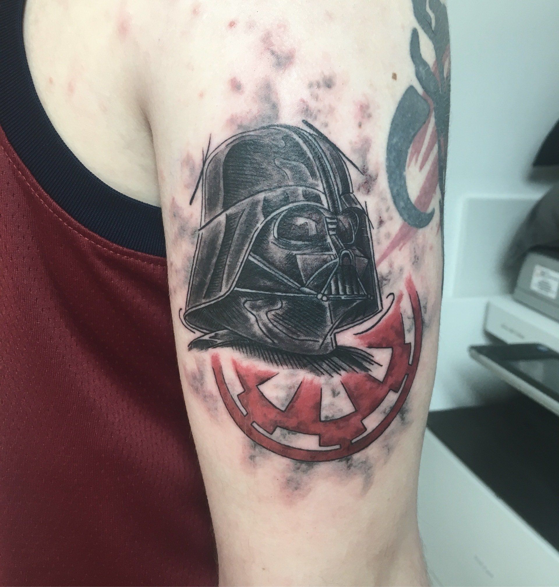Darth-Vader-Tattoo auf dem Arm, schwarzer Helm, rotes imperiales Symbol. Rote und graue Schattierungen, ein Star-Wars-Motiv.