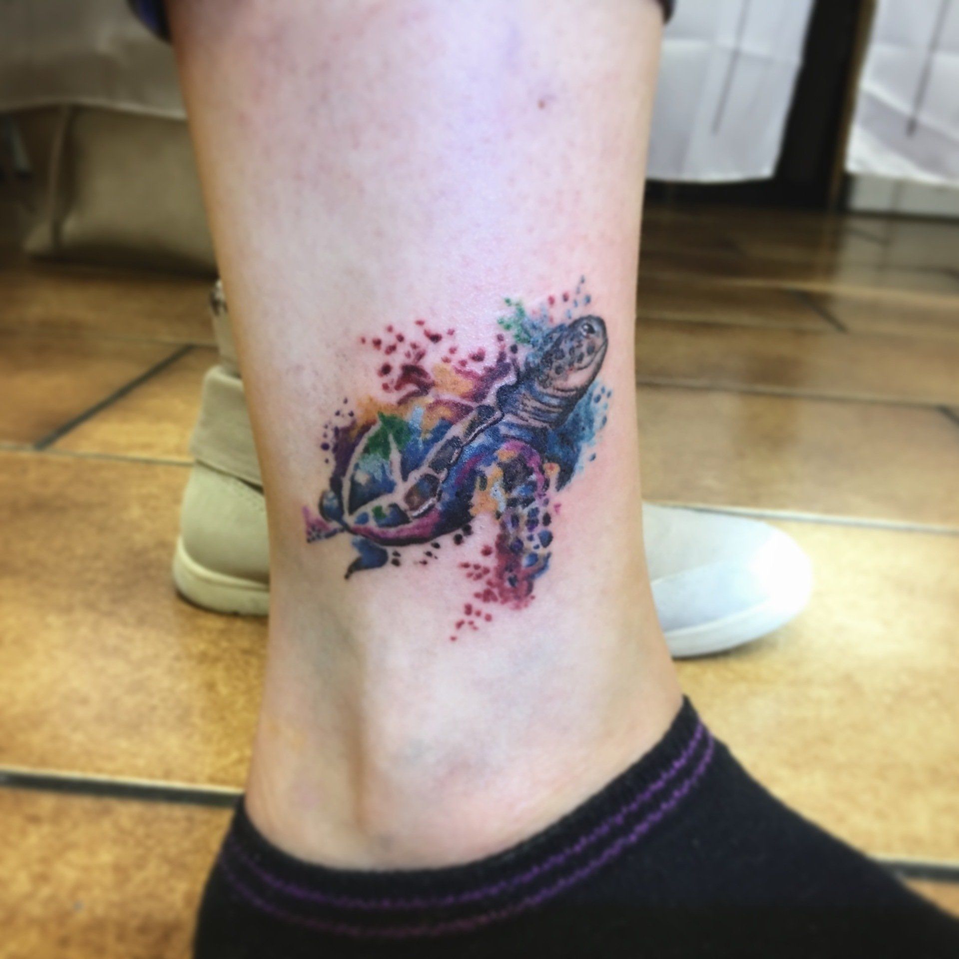 Aquarell-Meeresschildkröten-Tattoo am Knöchel mit bunten Farbspritzern.