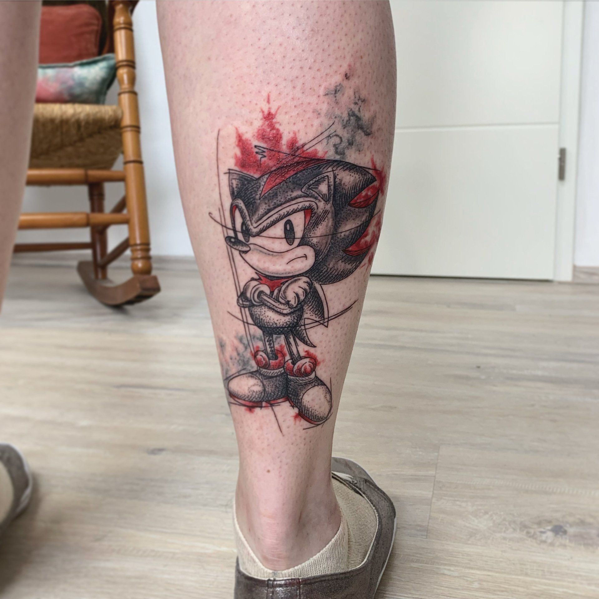 Tätowierung von Shadow the Hedgehog auf einem Bein, mit roten und grauen abstrakten Elementen.
