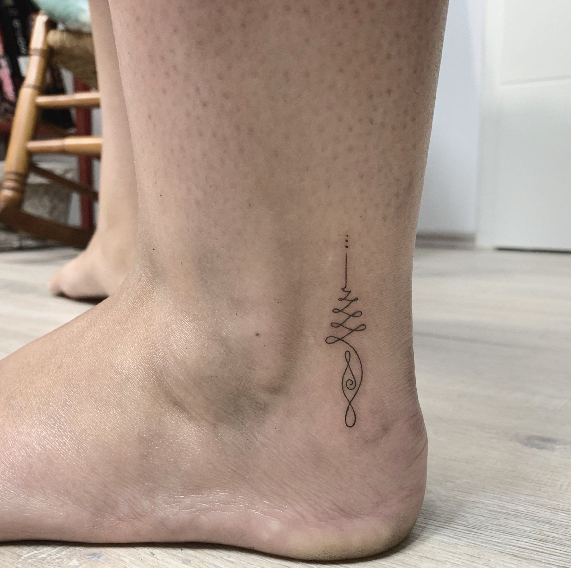 Knöcheltätowierung eines kleinen, dünnen, schwarzen Symbols auf dem Fuß einer Person, Haut sichtbar.