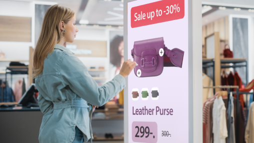 Woman interacts with a touchscreen display in a clothing store, viewing a purse with sale information.