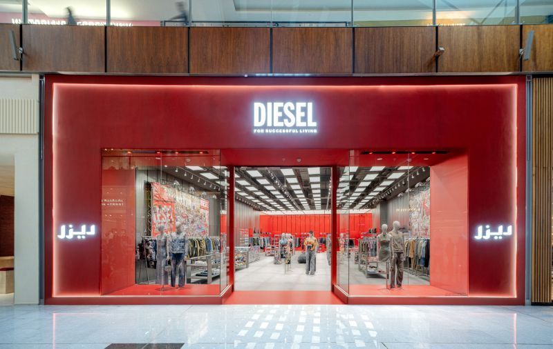 Diesel store front in red with open doors, displaying clothing and mannequins, with Arabic script on the right.