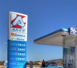 Gas station with tall blue and white ARGO sign, fuel prices, and gas pumps. A person stands nearby.