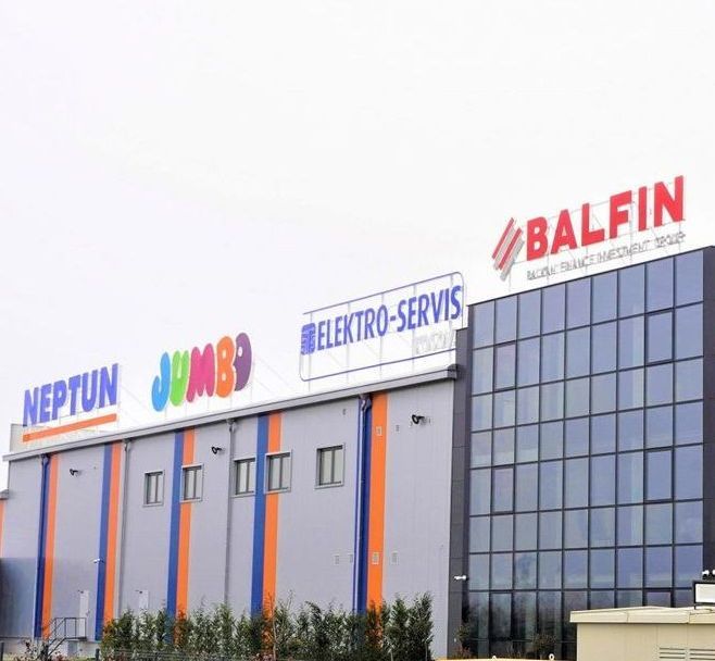 Building exterior with large signs for Neptun, Jumbo, Elektro-Servis, and Balfin. Colorful facade, cloudy sky.