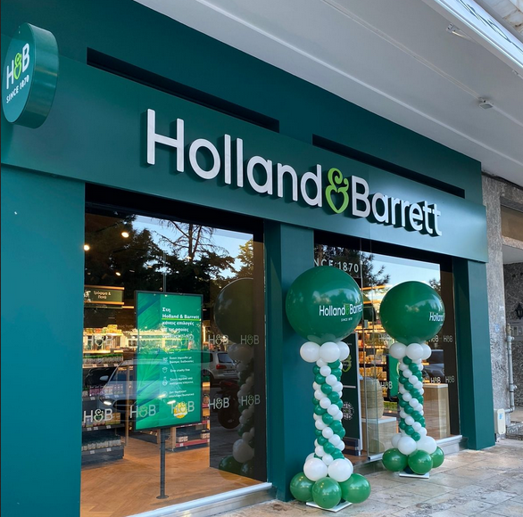 Holland & Barrett store front with green and white balloons. Green store sign with white text.