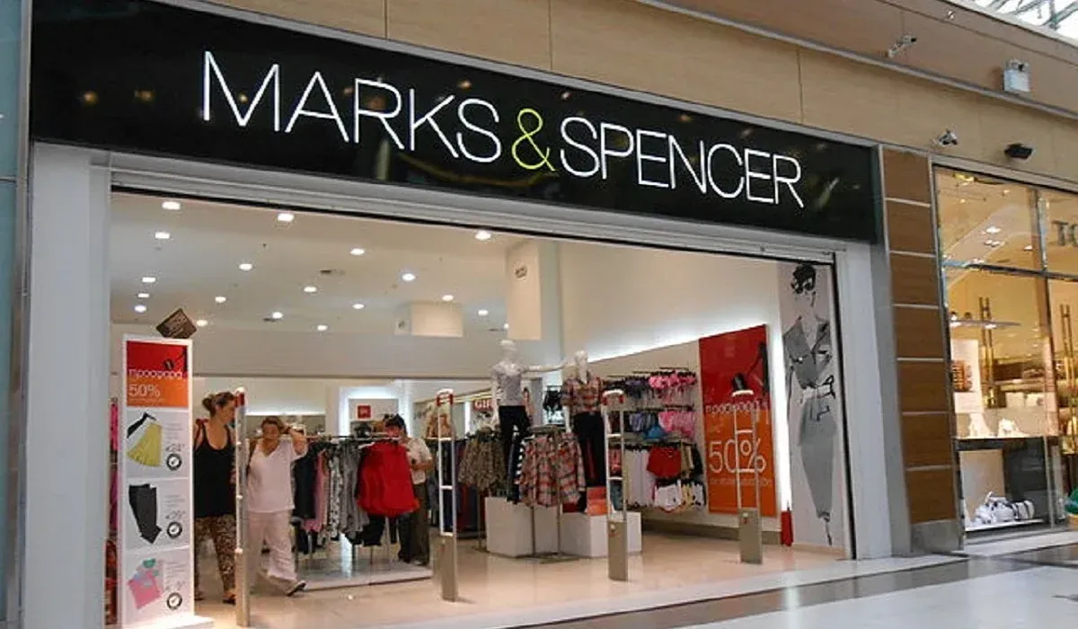 Marks & Spencer store entrance with clothing displayed. Shoppers browse inside the bright shop.