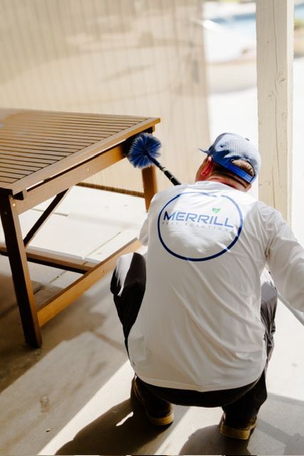 Worker kneeling beside a wooden table, cleaning or repairing it near a bright window.