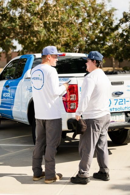 Two workers in white shirts and caps stand by a blue-and-white utility truck outdoors.