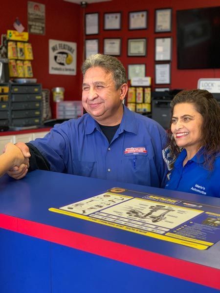 Two employees in blue shirts smiling behind a blue service counter in a red-walled shop | Mario’s Automotive