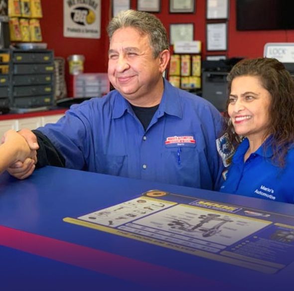 Two employees in blue shirts greeting a customer at a service counter with a document on the desk | Mario’s Automotive