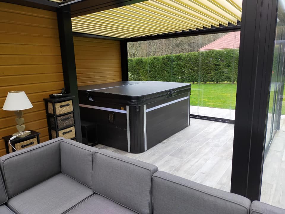 Un bain à remous est installé sous une pergola à côté d'un canapé.