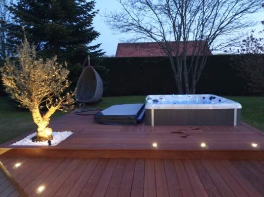 Une terrasse avec un jacuzzi et un arbre dessus