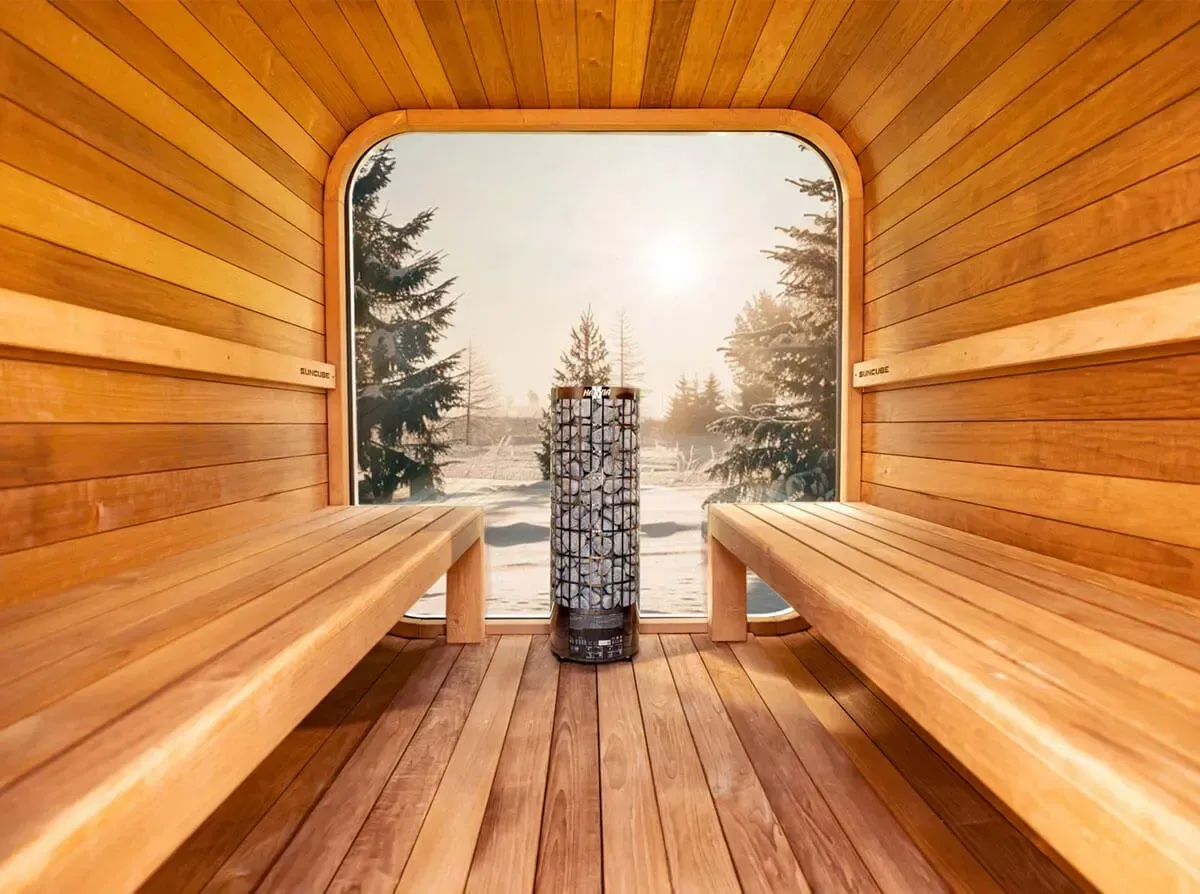Un sauna en bois avec des bancs et une fenêtre donnant sur une forêt enneigée.