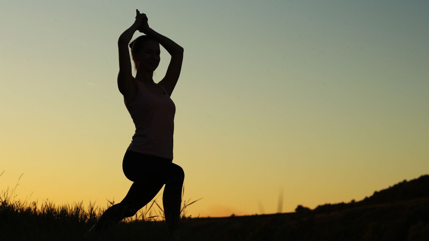 Une silhouette d'une femme faisant du yoga dans un champ au coucher du soleil.