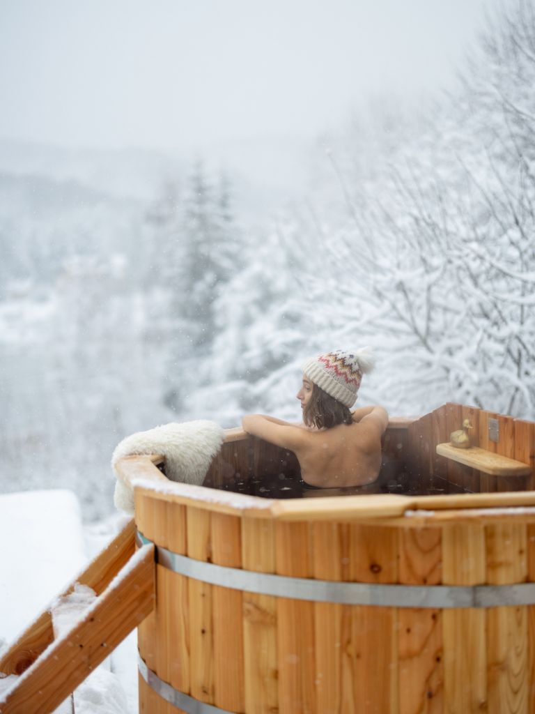 Une femme prend un bain dans une baignoire en bois sous la neige.