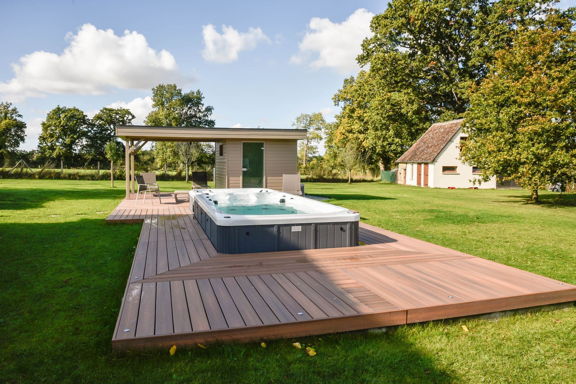 Un bain à remous est installé sur une terrasse en bois au milieu d'un champ verdoyant.