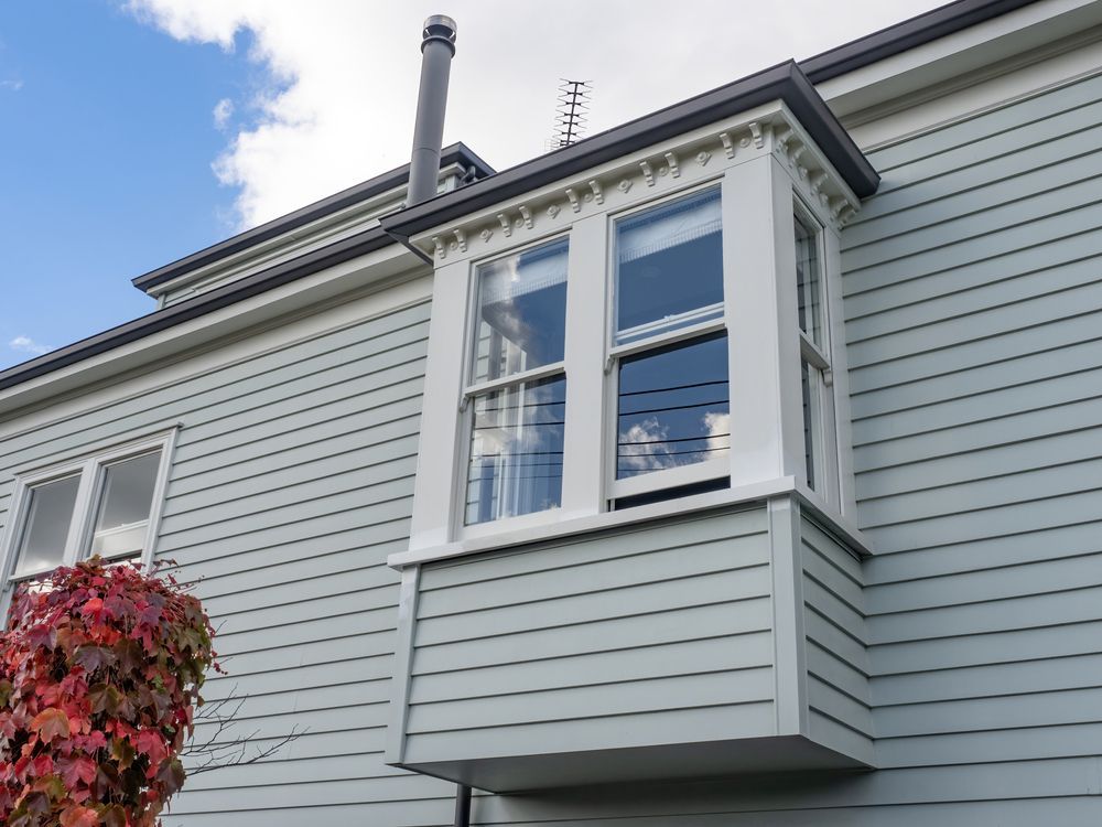 Light Blue House With White Trim Bay Window, Gray Siding, and a Red Bush — Working Windows in Mullumbimby, NSW
