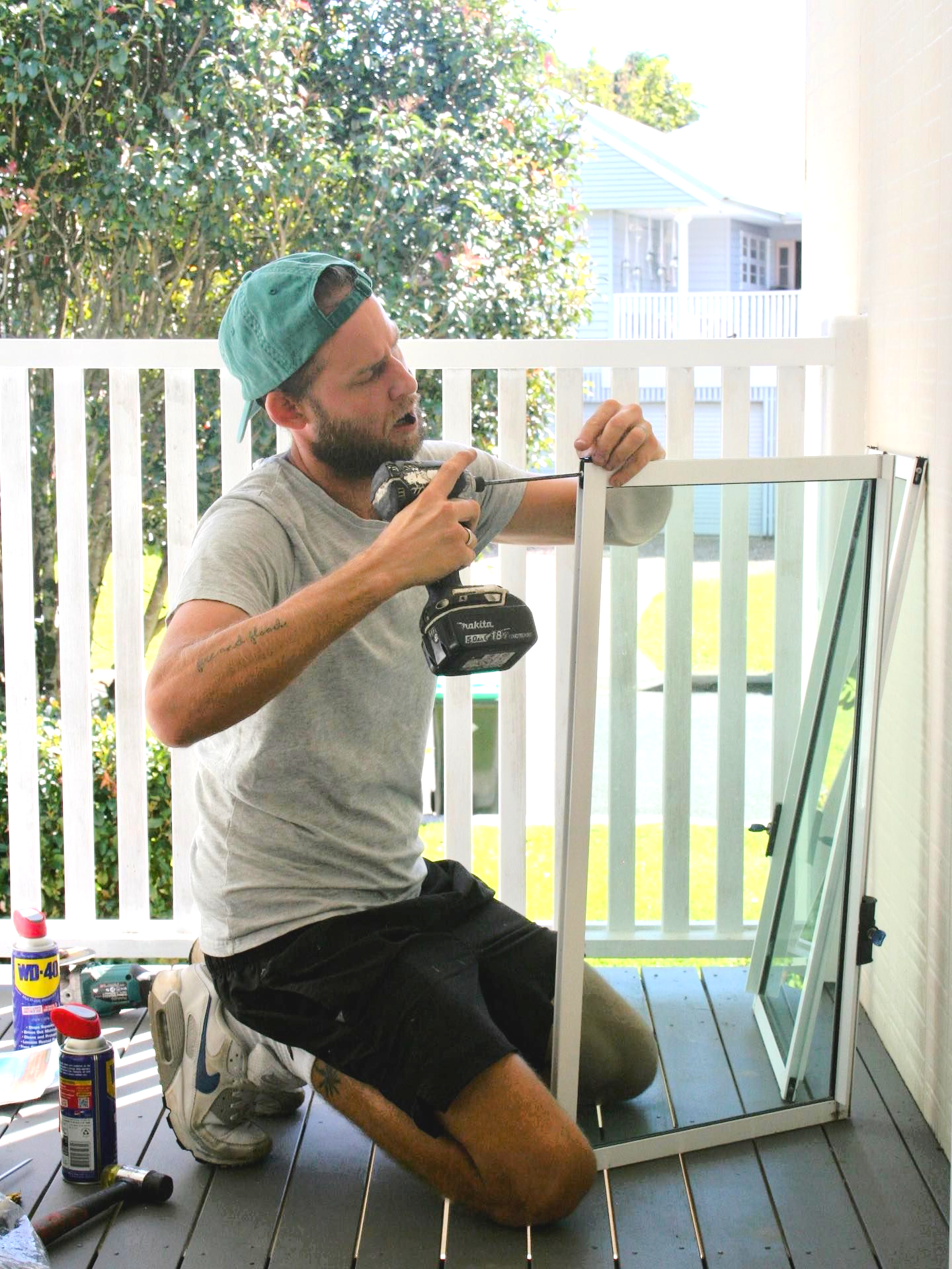 Man Kneeling, Using a Drill on a White Framed Window — Working Windows in Byron Bay, NSW