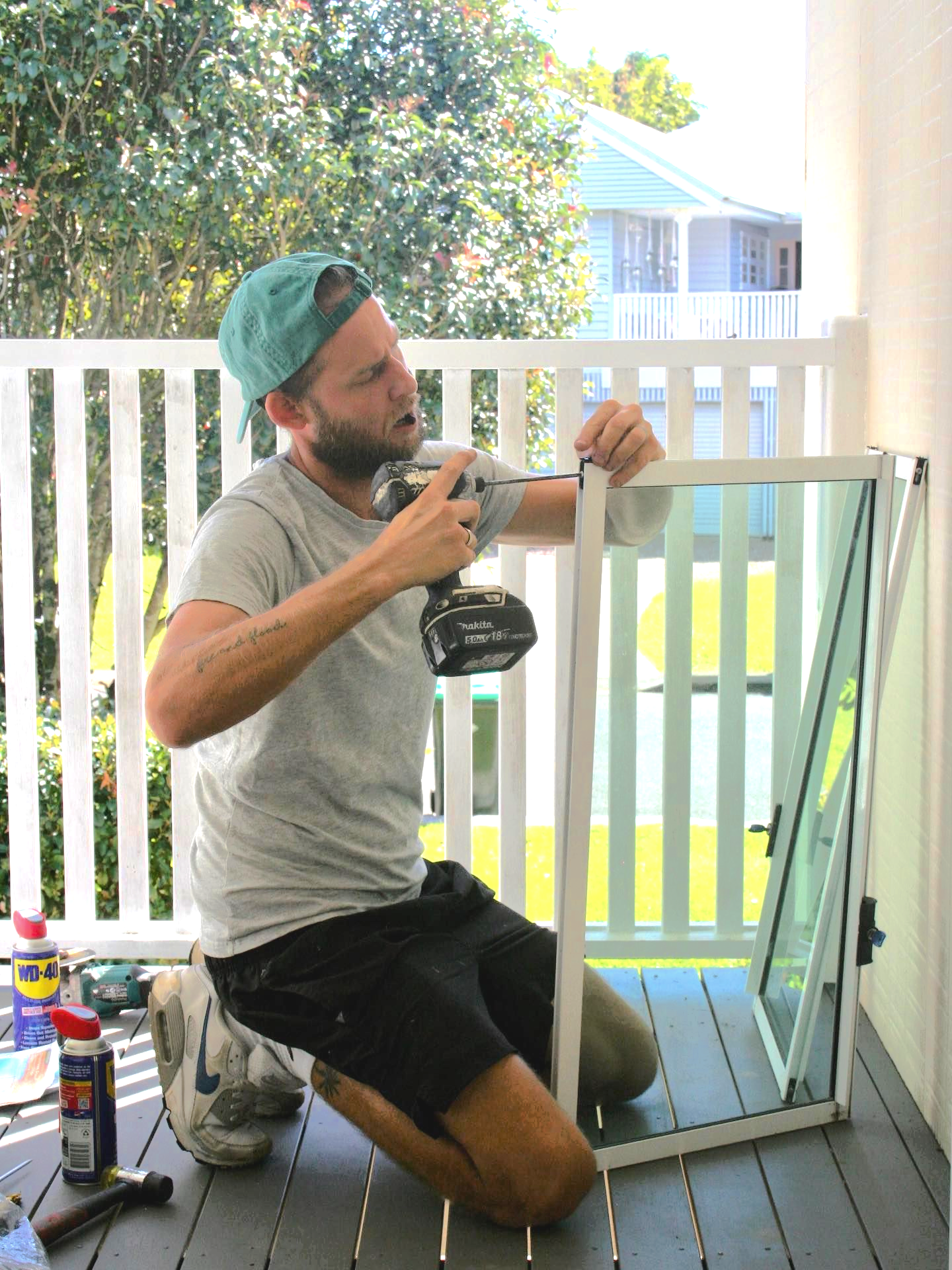 Man Kneeling on Deck, Using a Drill to Assemble a Window Frame — Working Windows in Byron Bay, NSW