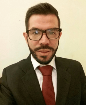 Un hombre con gafas y barba lleva traje y corbata.