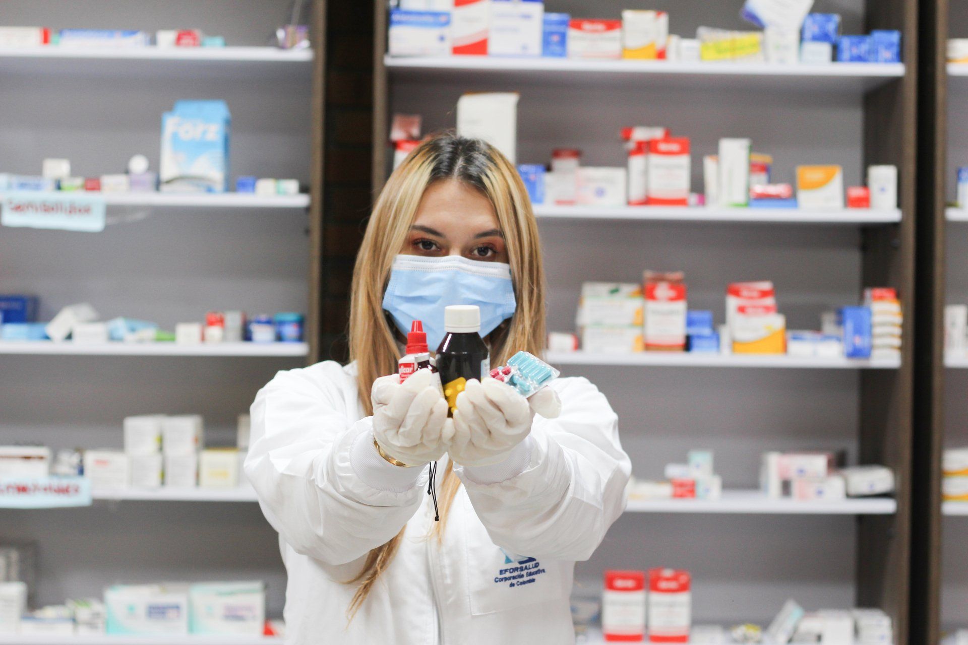 Una farmacéutica que lleva mascarilla y guantes sostiene un frasco de pastillas.