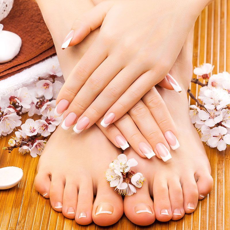 Un primer plano de las manos y los pies de una mujer con flores en el fondo.