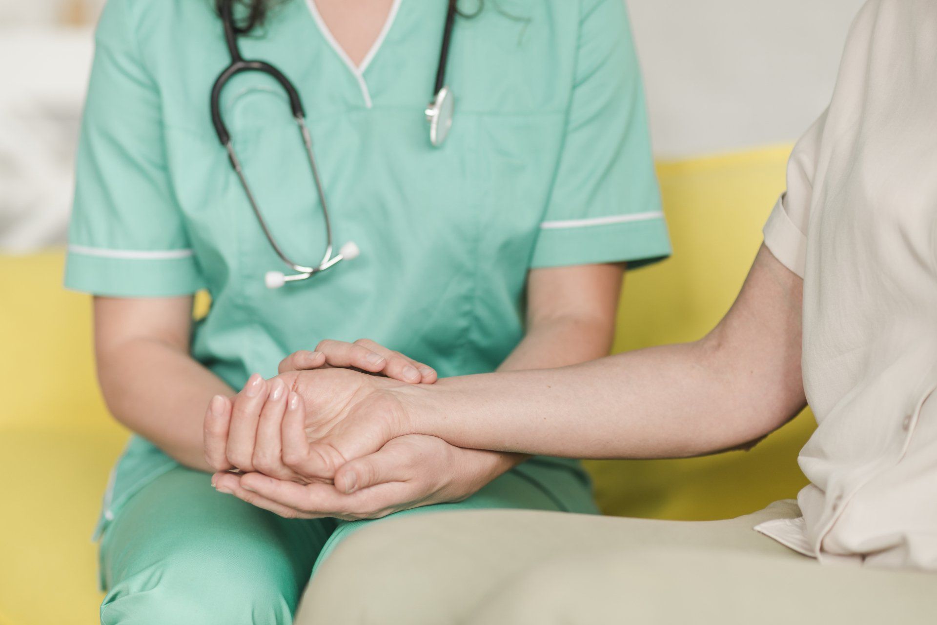Una enfermera sostiene la mano de un paciente mientras está sentada en un sofá.