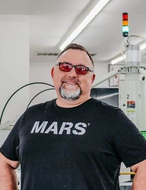 Man with glasses and beard wearing a black MARS t-shirt in a manufacturing facility.