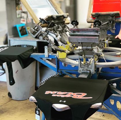 Screen printing machine printing a black shirt with a red and white logo in a workshop.