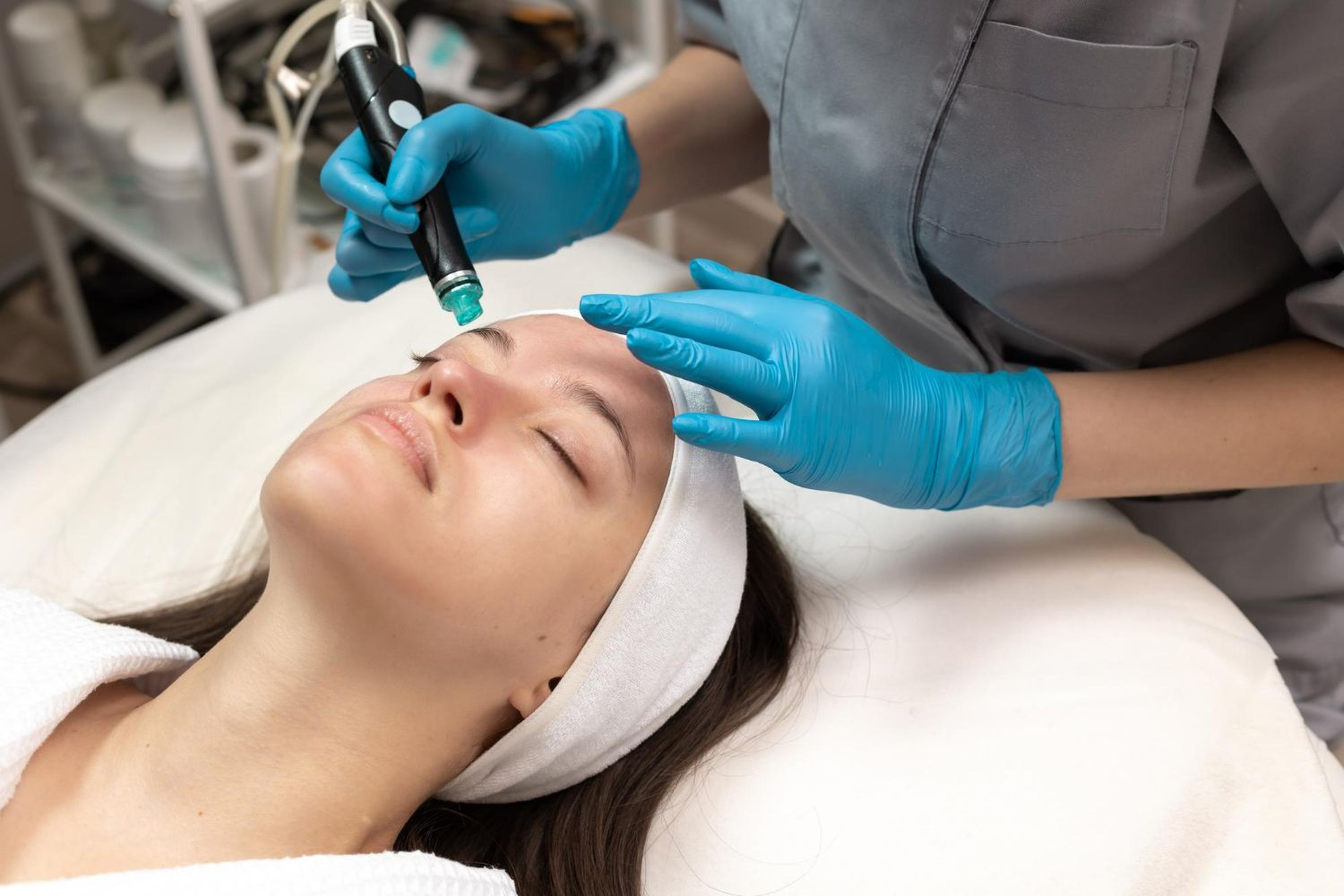 A person in blue gloves performs a hydrafacial treatment on a client's face at a spa.