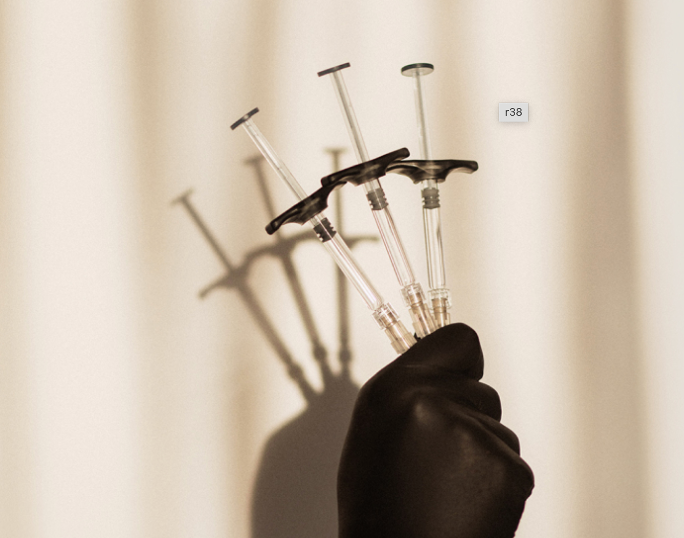 A hand in a black glove holds three syringes against a light, neutral background, casting long shadows.